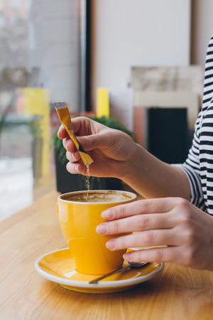 Girl pours sugar from a bag into a mug of coffee. Selective focus. Toning.の写真素材