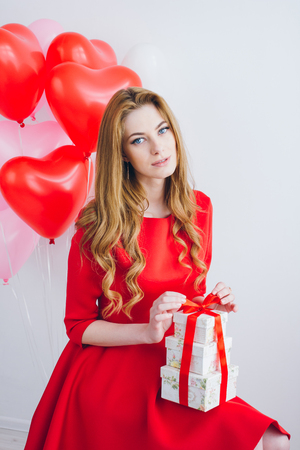 Beautiful girl in red dress with balloons in the shape of a heart holds boxes with gifts. The concept of love, Valentine's day. Toning.の写真素材