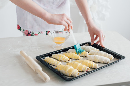 Young beautiful woman preparing homemade croissants. Housewife lubricate croissants egg and sprinkle with sugar. The concept of home cooking. Toning.の写真素材