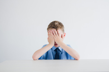 Schoolboy in school uniform covers his face from exhaustion. Toning.の写真素材