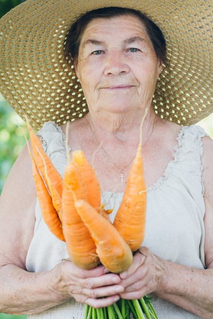 Portrait of an elderly woman in a hat holding a carrot. Toning. Selective focus.の写真素材