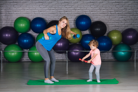 Young sporty mother and baby girl do exercises together in the gym. Parent and child healthy development, fitness and relaxation. Healthy lifestyle concept photo. Toning.の写真素材