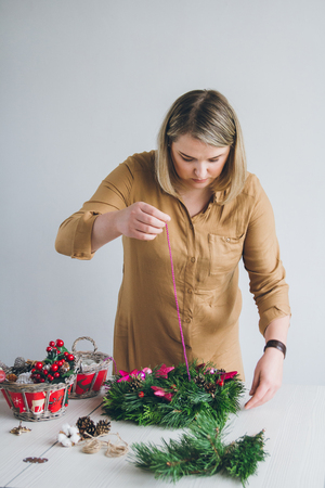 Florist decorator making Christmas wreath handmade on a white table. Women's hobby. Preparations for the holidays concept.の写真素材