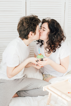 Couple in love celebrates the holiday in bed over a sweet Breakfast. Blowing out candles on cupcakes. The concept of love and romance. Toning.の写真素材