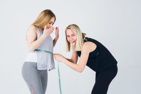 Slender girl athlete measures the size of the belly of her pregnant girlfriend and surprised. The...