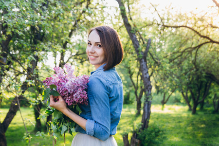 Young beautiful brunette girl posing with a bouquet of lilac in a summer Apple orchard. The concept of a family holiday. Toning.の写真素材