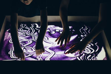 Sand animation. A young beautiful woman and a boy draw with their fingers on an interactive sand table. Training master class.の写真素材
