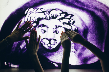 Sand animation. A young beautiful woman and a boy draw with their fingers on an interactive sand table. Training master class.の写真素材