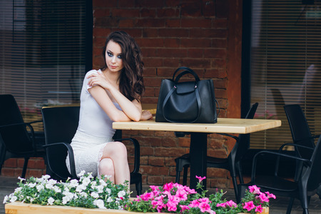 Young beautiful brunette girl with long hair in elegant white dress. Woman walking through the streets of the city in the evening at sunset.の写真素材