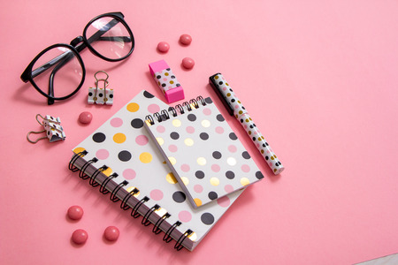 Notepad, pen and glasses on pink background. Flat ley composition. Office supplies on the table.の写真素材