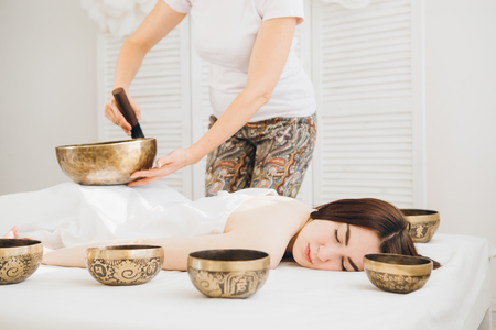 Young beautiful girl doing massage therapy singing bowls in the Spa. The concept of relaxation and alternative medicine. Toning.の写真素材