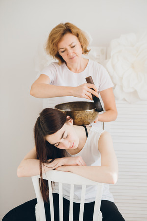 Young beautiful girl doing massage therapy singing bowls in the Spa. The concept of relaxation and alternative medicine. Toning.の写真素材