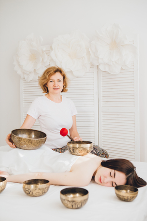 Young beautiful girl doing massage therapy singing bowls in the Spa. The concept of relaxation and alternative medicine. Toning.の写真素材