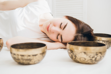 Young beautiful girl doing massage therapy singing bowls in the Spa. The concept of relaxation and alternative medicine. Toning.の写真素材