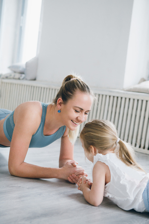 Young sporty mother and baby girl do exercises together in the gym. Parent and child healthy development, fitness and relaxation. Healthy lifestyle concept photo. Toning.の写真素材