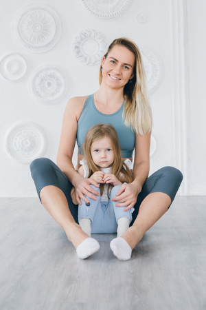 Young sporty mother and baby girl do exercises together in the gym. Parent and child healthy development, fitness and relaxation. Healthy lifestyle concept photo. Toning.の写真素材