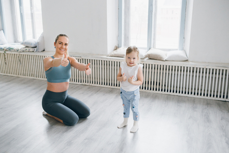 Young sporty mother and baby girl do exercises together in the gym. Parent and child healthy development, fitness and relaxation. Healthy lifestyle concept photo. Toning.の写真素材