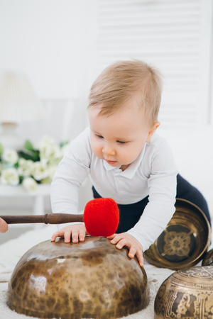 Little boy playing with Tibetan singing bowls sitting on the bed. Sound therapy for the baby. Toning.の写真素材