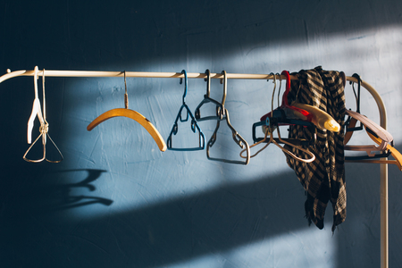 Various hangers hang on a rack at a blue wall in the sun. Toning.の写真素材