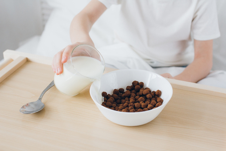 Cute boy eating Breakfast chocolate balls sitting in bed with white linensの写真素材