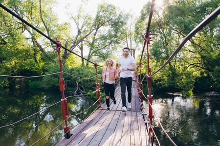 Young couple guy and girl running on the bridge over the river fooling around in the summer at sunset. The concept of freedom, love and family. Toning.の写真素材