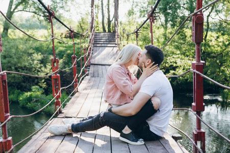 Young couple guy and girl on the bridge over the river and kiss in summer at sunset. The concept of freedom, love and family. Toning.の写真素材