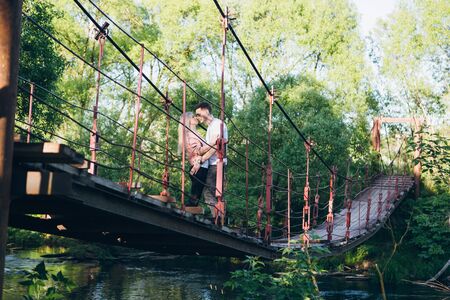 Young couple guy and girl on the bridge over the river and kiss in summer at sunset. The concept of freedom, love and family. Toning.の写真素材