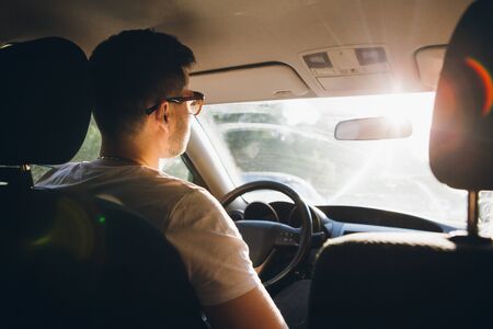 Young man driving a car in the setting sun. Toning.