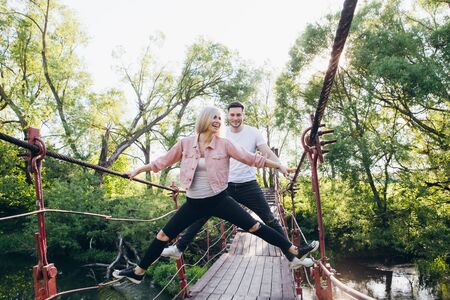Young couple guy and girl on the bridge over the river fooling around in the summer at sunset. The concept of freedom, love and family. Toning.の写真素材