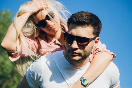 Young beautiful girl sitting on the back of a man hugging and smiling in nature in summer. The concept of freedom, love and family. Toning.の写真素材