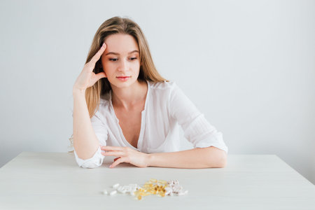 Young beautiful girl chooses pills. Colorful capsules of tablets, vitamins, dietary supplements are on the table. Toning.の写真素材