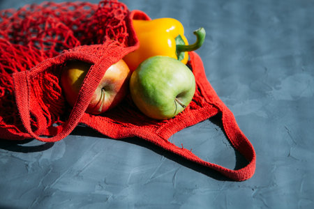 Red mesh reusable shopping bag the shopping bag with the apples and peppers on a gray background....