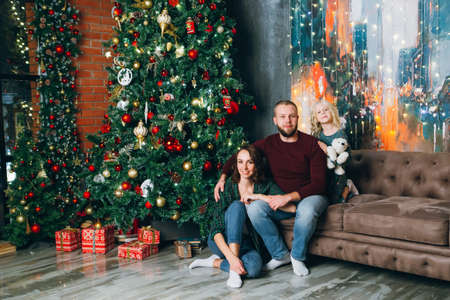 Cute family mom, dad and daughter pose at the Christmas tree. Happy new year concept. Toning.の写真素材