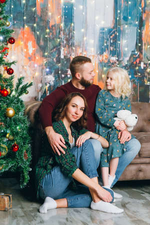 Cute family mom, dad and daughter pose at the Christmas tree. Happy new year concept. Toning.の写真素材