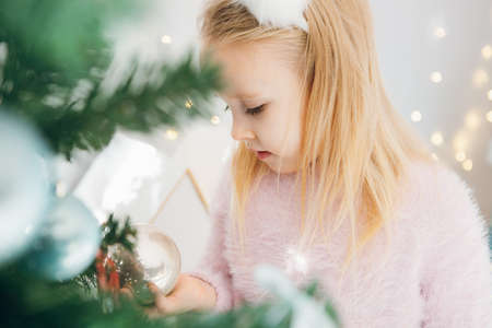 Cute little girl with blonde hair is decorating a Christmas tree. The holiday concept. Toning.の写真素材