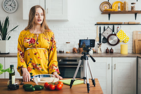 Young pretty pregnant girl blogger shoots a video of a salad recipe on a smartphone camera. The concept of healthy eating. Toning.の写真素材