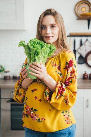 Young cute pregnant girl preparing vegetable salad in the kitchen. The concept of healthy eating. Toning.の写真素材