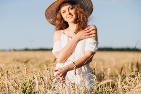 Young beautiful girl with long curly hair poses in a wheat field in the summer at sunset. The girl...