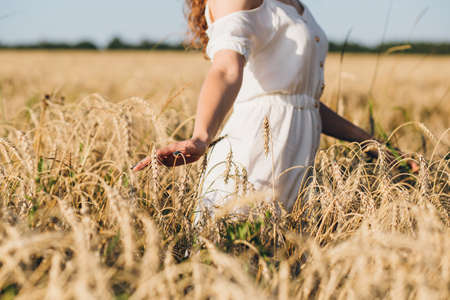 Young beautiful girl with long curly hair poses in a wheat field in the summer at sunset. The girl in the hat. Toning.の写真素材