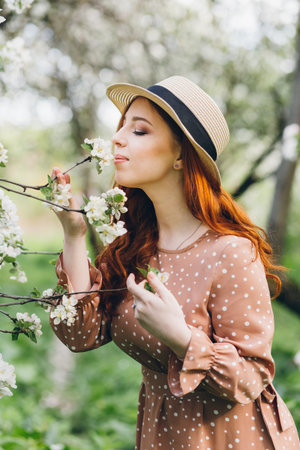 Young beautiful red-haired girl walks in a spring blooming apple orchard. Tinting.の写真素材