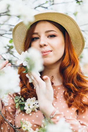 Young beautiful red-haired girl walks in a spring blooming apple orchard. Tinting.