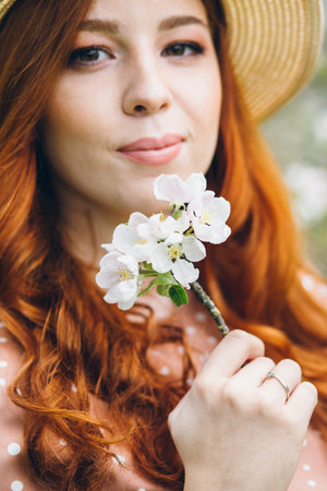 Young beautiful red-haired girl walks in a spring blooming apple orchard. Tinting.