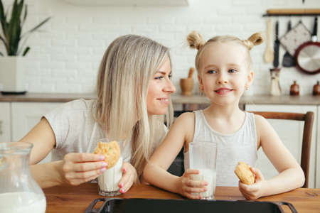 Cute little girl and mom eating freshly baked cookies with milk in the kitchen. Happy family. Toning.の写真素材