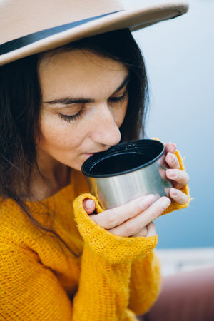 Young woman sits on a bridge on a lake with an autumn landscape and drinks hot tea from a flask. Toning.の写真素材