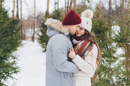 Young beautiful couple embraces in a winter coniferous forest. A park with Christmas trees on the background. Christmas mood. Tinting.の写真素材
