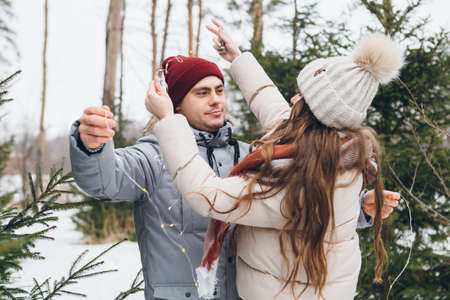 Young beautiful couple in love hugs and kisses in a winter coniferous forest. A park with Christmas trees on the background. Christmas mood. Tinting.の写真素材