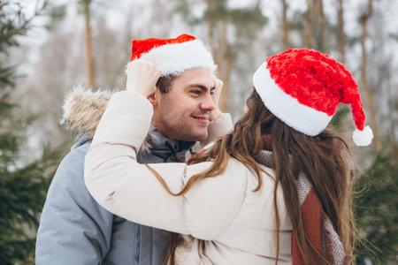 Young beautiful couple in a Santa hat and hugging and fooling around in a winter coniferous forest. Park with fir trees on the background. Christmas mood. Tinting.の写真素材