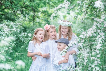 Four laughing children in white summer clothes in a blooming gardenの写真素材