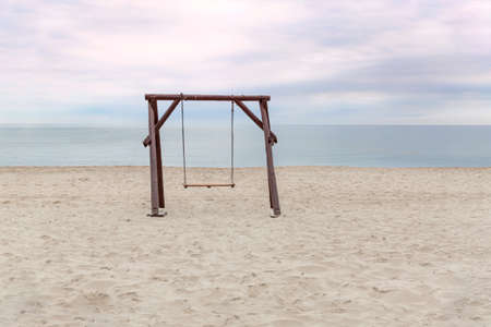 A large wooden swing on an empty beach against the background of the sea and skyの写真素材