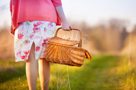 A young woman walks along the road to the field and carries a wicker basket with grass in her hands.の写真素材